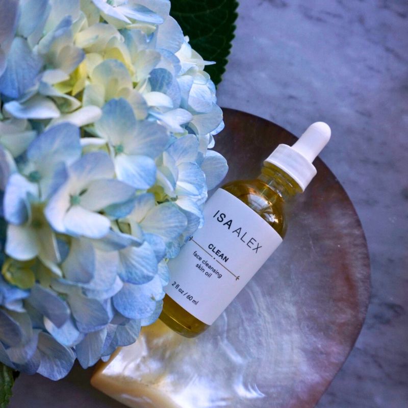 ISA ALEX skincare oil bottle with dropper on a wooden surface next to blue hydrangeas