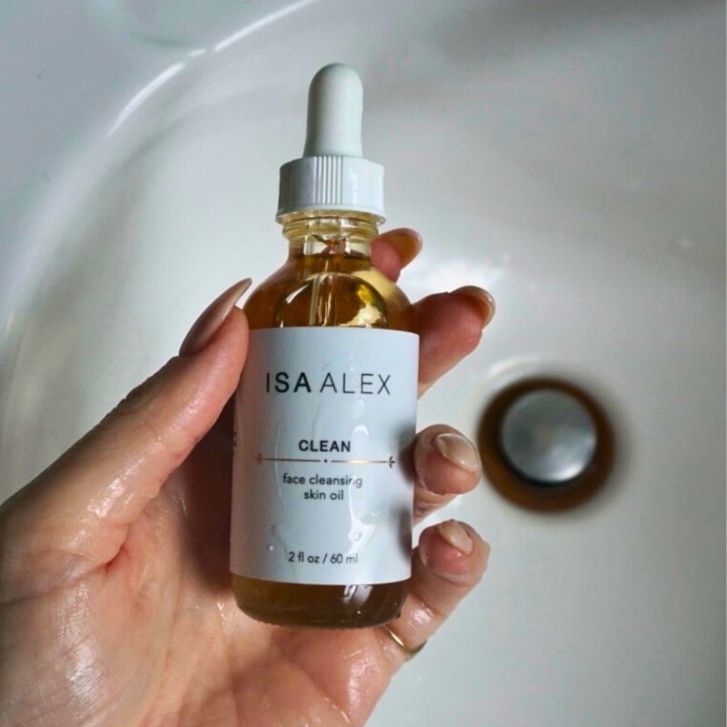 Hand holding a bottle of Isa Alex skincare oil over a sink.