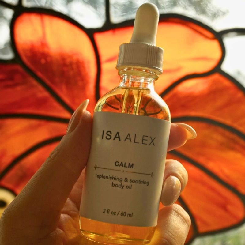 Bottle of ISA ALEX Calm body oil held in front of a butterfly wing.