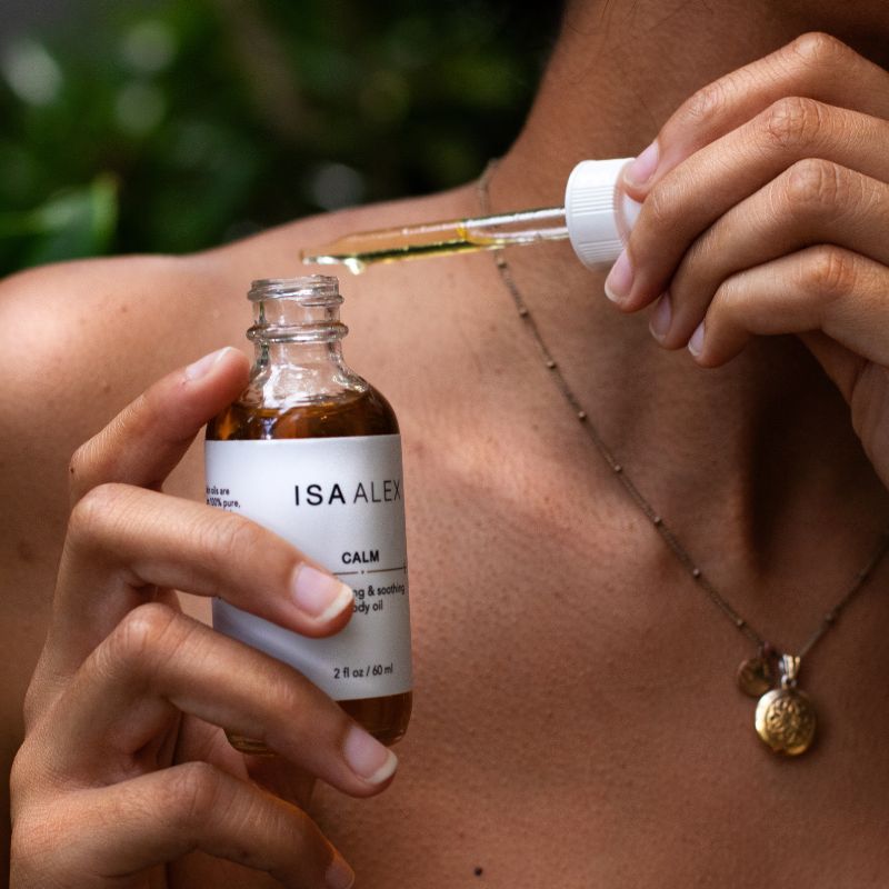 Person applying ISA ALEX oil to their shoulder with a dropper.